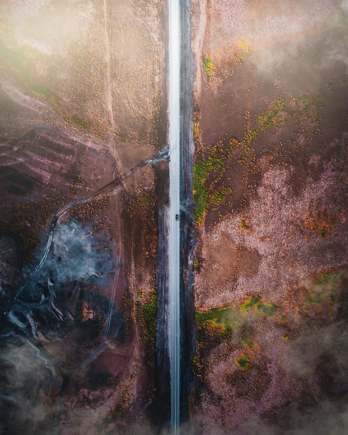 Auto fährt auf schmaler Straße durch weite, spärlich bewachsene Landschaft.